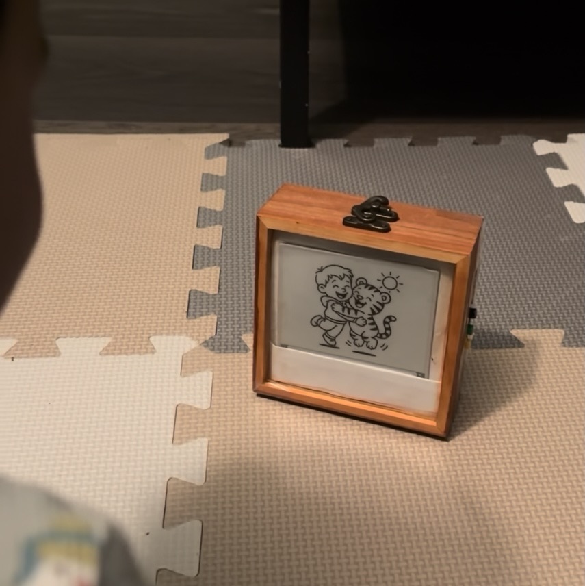 An early handmade Tinku in a wooden case, a boy-and-tiger line drawing on its display, resting on a child's play mat