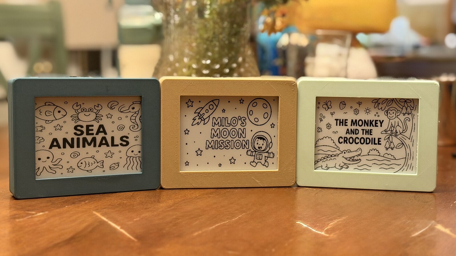 Three finished Tinku players in blue, yellow, and green, showing Sea Animals, Milo's Moon Mission, and The Monkey and the Crocodile